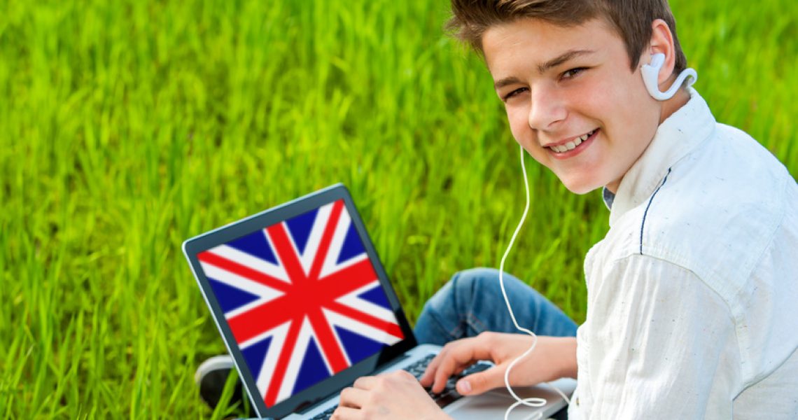 Portrait of attractive teen boy learning english on laptop outdoors.